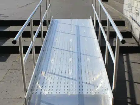 Aluminium-Rampe mit rutschfester Oberfläche, die einen barrierefreien Zugang zu einem  erhöhten Bereich ermöglicht. Sideschutz durch Geländer.