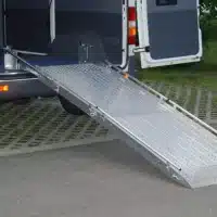 Aluminium-Rampe für den Zugang zu einem Fahrzeug, ausgeklappt und auf Bodenhöhe, mit rutschfester Oberfläche und seitlichen Führungsschienen.