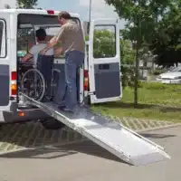 Fahrer hilft einem Rollstuhlfahrer beim Einsteigen in einen behindertengerechten Bus mit Rampe.