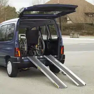 Ein blauer Vans mit offenen Heckklappen, der eine Rampe zeigt, die für den Zugang eines Rollstuhls ins Fahrzeug dient. Im Inneren steht ein Rollstuhl auf der Rampe.