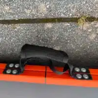 Handgriff in einer zusammengeklappten Rollstuhlrampe mit orangefarbenen Kante, fotografiert auf Steinboden.