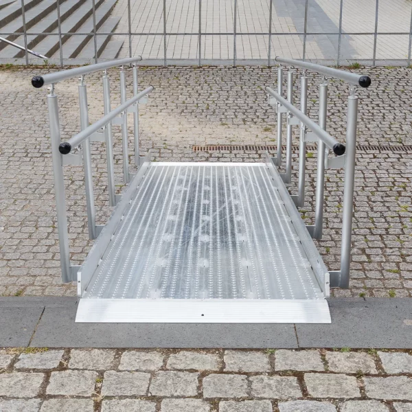 Eine Rollstuhlrampe aus Metall mit Handläufen auf beiden Seiten