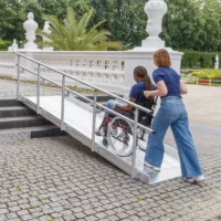 Eine Person im Rollstuhl benutzt eine Rollstuhlrampe auf einem Kopfsteinpflaster.