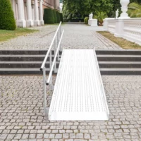 Eine Rollstuhlrampe aus Metall mit Geländer führt über eine Steintreppe auf einen Vorplatz im Freien.