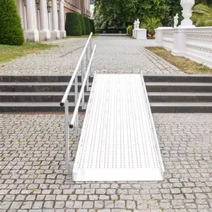 Eine Rollstuhlrampe aus Metall mit Geländer führt über eine Steintreppe auf einen Vorplatz im Freien.