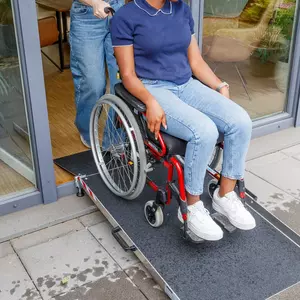 Eine Person im Rollstuhl wird von einer anderen Person über eine tragbare Rampe an einer Türöffnung geschoben.