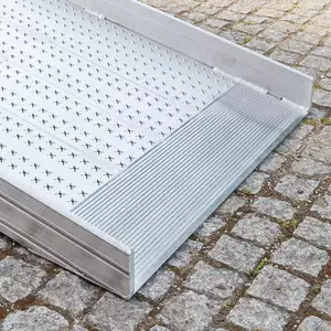 Eine Rollstuhlrampe aus Metall mit einer strukturierten Oberfläche ist mit der unteren Auflage auf einem Kopfsteinpflaster platziert.