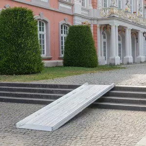 Vor einem historischen Gebäude mit beschnittenen Sträuchern ist eine Rollstuhlrampe über Steinstufen angebracht.