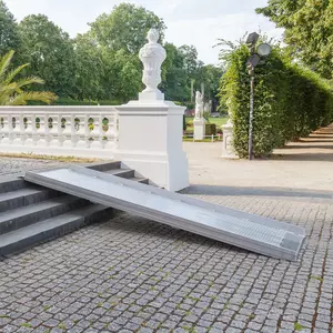 Eine Rollstuhlrampe ist über Steinstufen im Freien neben einem weißen Geländer und einer Statue in einer Parkanlage angebracht.