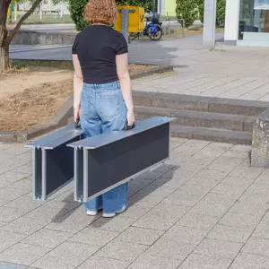 Eine Person mit lockigem Haar trägt eine zweiteilige Rollstuhlrampe