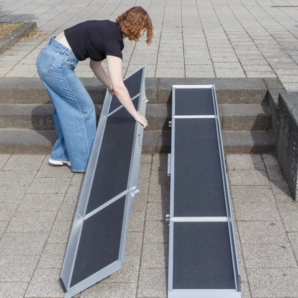 Eine Person klappt eine tragbare Rampe neben einer Treppe auf einer gepflasterten Außenfläche aus