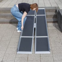 Eine Person baut eine tragbare Rampe auf einer Außentreppe auf und stellt sie auf einen gepflasterten Gehweg.