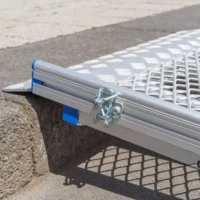 Eine Rollstuhlrampe aus Aluminium mit einer Klemme ist auf einer Treppenstufe angebracht.
