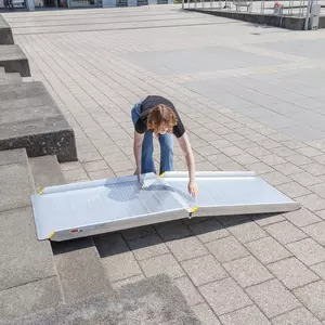 Eine Person legt eine tragbare Aluminium-Rollstuhlrampe auf Betonstufen im Freien auf.