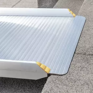 Nahaufnahme des oberen Auflagewinkels einer Rollstuhlrampe mit gelben Eckschützern. Dieser liegt auf einer Betonstufe auf.