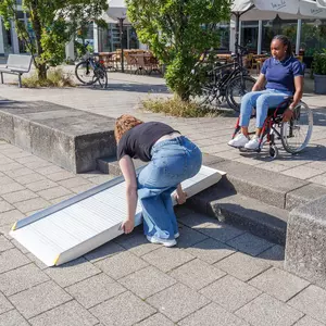 Eine Person richtet eine tragbare Aluminium-Rollstuhlrampe auf einer Treppe aus 2 Stufen aus