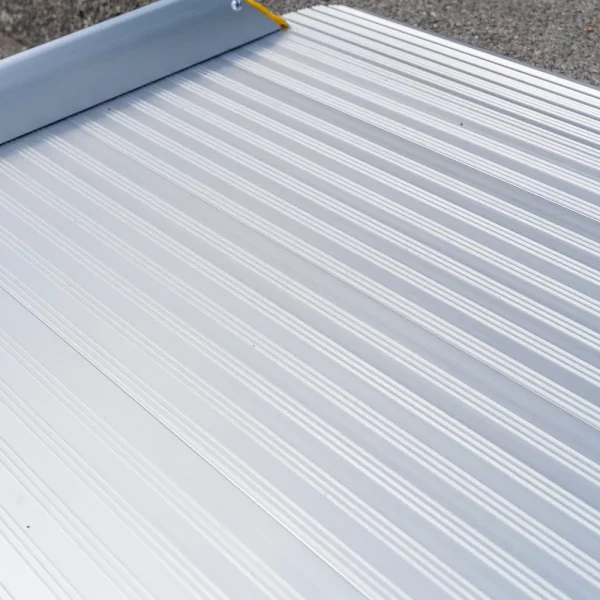 Nahaufnahme der rutschsicher geriffelten Fahrfläche einer Rollstuhlrampe aus Aluminium auf einer Betonfläche