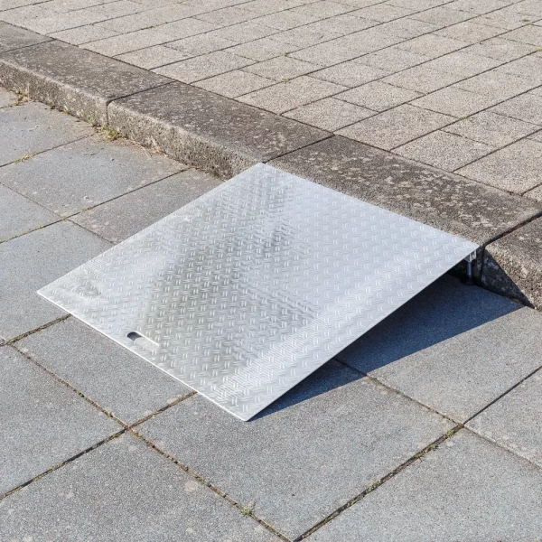 Eine Rollstuhlrampe aus Aluminium auf einem Bordstein ermöglicht den Zugang zwischen dem Gehweg und dem höher gelegenen Bürgersteig.