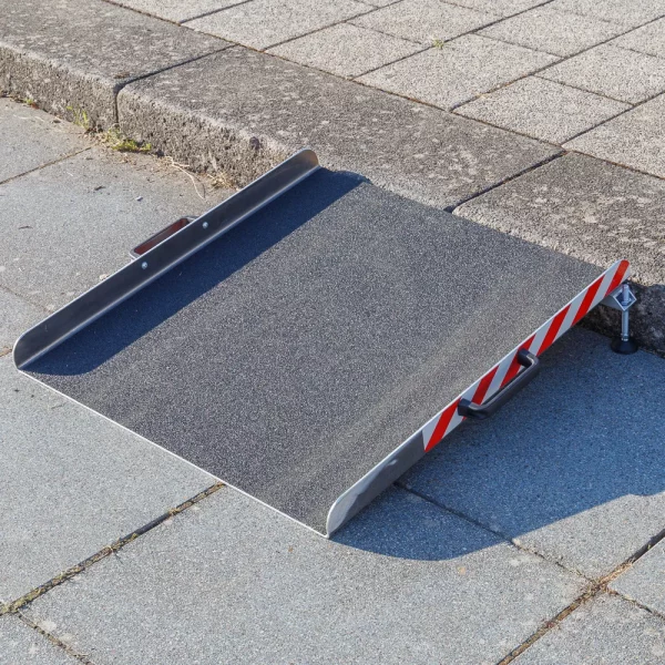 Eine tragbare Rollstuhlrampe aus Alumnium steht vor einer einzelnen Stufe