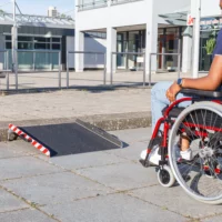 Eine Person im Rollstuhl nähert sich einer tragbaren Rollstuhlrampe aus Aluminium