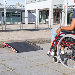 Eine Person im Rollstuhl nähert sich einer tragbaren Rollstuhlrampe aus Aluminium