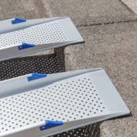 Nahaufnahme des oberen Auflagewinkels von 2 Schienen einer Rollstuhlrampe mit blauem Kantenschutz und rutschsicherer Fahrfläche. Diese liegen auf der Kante einer Stufe