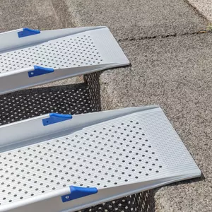 Nahaufnahme des oberen Auflagewinkels von 2 Schienen einer Rollstuhlrampe mit blauem Kantenschutz und rutschsicherer Fahrfläche. Diese liegen auf der Kante einer Stufe