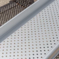 Nahaufnahme der Fahrfläche einer Rollstuhlrampenschiene mit gelochter und längsgeriffelter Oberfläche mit Unterbrechung der Riffel. Die Rampe ist aus Aluminium.