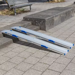 Zwei tragbare Rollstuhlrampen- Schienen liegen über einer Treppe aus 2 Stufen auf einem gepflasterten Gehweg im Freien.