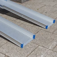Nahaufnahme von zwei unteren Enden der Schienen einer Rollstuhlrampen aus Aluminium liegen an einem sonnigen Tag im Freien auf einer gepflasterten Fläche.