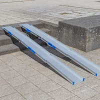 Zwei tragbare Rollstuhlrampen Schienen liegen auf einer Außentreppe und ermöglichen den Zugang zwischen verschiedenen Ebenen einer gepflasterten Fläche.