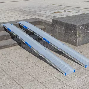 Zwei tragbare Rollstuhlrampen Schienen liegen auf einer Außentreppe und ermöglichen den Zugang zwischen verschiedenen Ebenen einer gepflasterten Fläche.