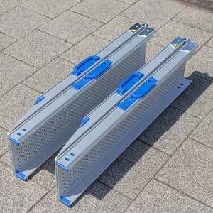 Zwei zusammen geklappte und zusammen geschobene Rollstuhlrampen Schienen aus Aluminium liegen nebeneinander auf einer gepflasterten Fläche.