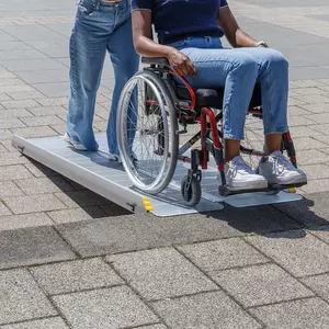 Zwei Personen benutzen eine tragbare Rollstuhlrampe; eine sitzt in einem Rollstuhl