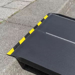 Nahaufnahme des oberen Auflagewinkels einer tragbaren schwarzen Rollstuhlrampe mit gelben und schwarzen Streifen wird auf einer Stufenkante