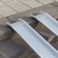 Zwei nebeneinander liegende Schienen einer Rollstuhlrampe aus Aluminium liegen auf Steinstufen im Freien