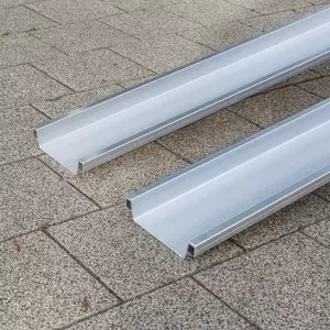 Detailaufnahme der unteren Auflagenfläche von zwei Schienen einer Rollstuhlrampe aus Metall auf einer gepflasterten Außenfläche.