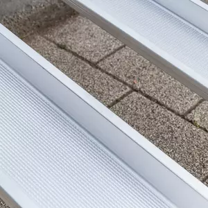 Nahaufnahme von zwei Schienen einer Aluminium-Rollstuhlrampe mit geriffelter Fahrfläche über einer Treppe im Außenbereich.
