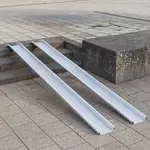 Zwei Schienen einer Rollstuhlrampe aus Aluminium ist über einer Betontreppe im Außenbereich platziert.