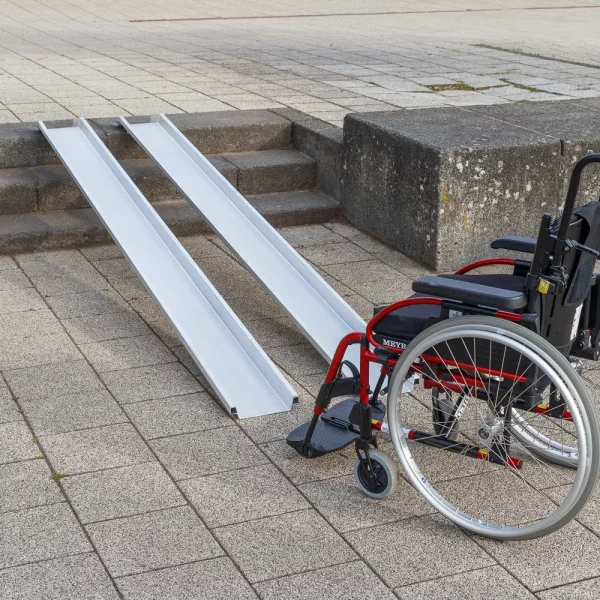 Ein roter Rollstuhl steht am unteren Ende von zwei Schienen einer Rollstuhlrampe