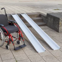 Ein roter Rollstuhl steht links neben zwei Schienen einer Rollstuhlrampe