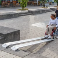 Eine Frau im roten Rollstuhl am unteren Ende einer Schienenrampe über Treppen im Außenbereich