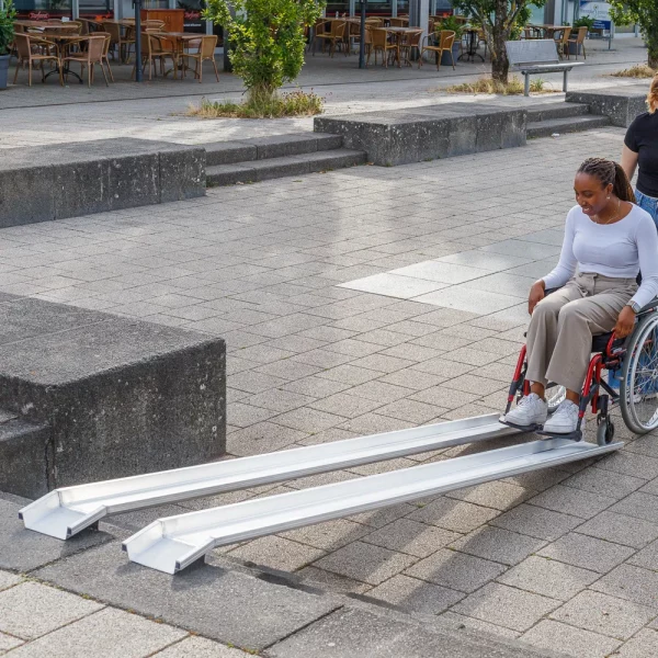 Eine Frau im roten Rollstuhl am unteren Ende einer Schienenrampe über Treppen im Außenbereich