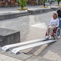 Eine Frau im roten Rollstuhl am unteren Ende einer Schienenrampe aus Aluminium über Treppen im Außenbereich