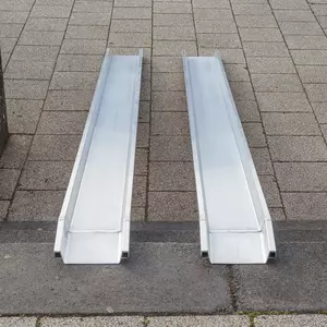 Zwei parallel platzierte tragbare Aluminiumschienen einer Rollstuhlrampe über Treppenstufen im Außenbereich von der oberen Stufe aus fotografiert.