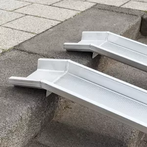 Detailaufnahme der oberen Auflagefläche von zwei parallel platzierten Schienen einer Rollstuhlrampe aus Aluminium über einer Betontreppe platziert.