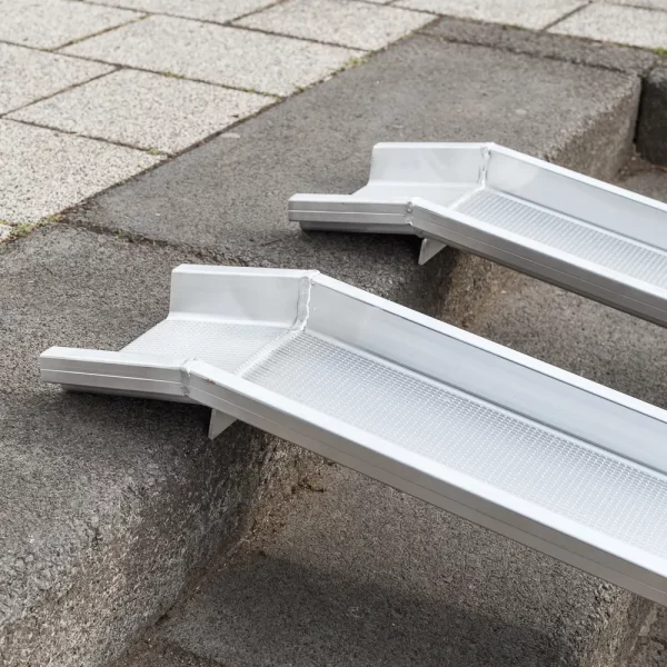Detailaufnahme der oberen Auflagefläche von zwei parallel platzierten Schienen einer Rollstuhlrampe aus Aluminium über einer Betontreppe platziert.