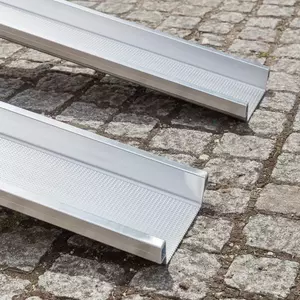 Detailaufnahme des unteren Endes von zwei parallel platzierten Schienen einer mobilen Rollstuhlrampe mit strukturierter Oberfläche auf Kopfsteinpflaster..