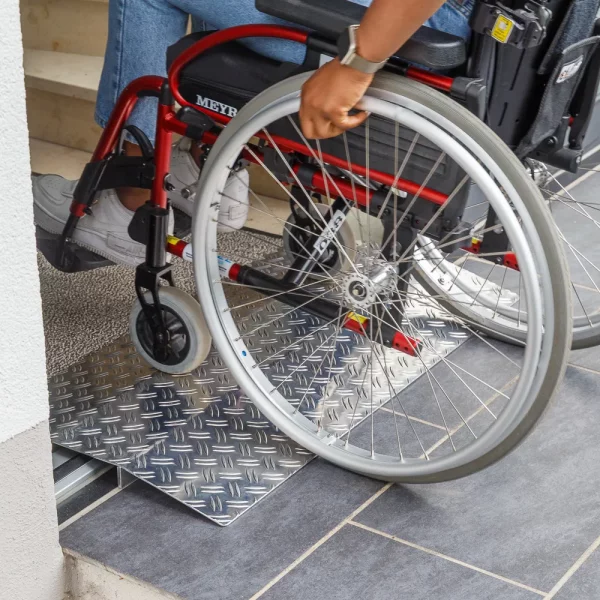 Eine Person im Rollstuhl benutzt eine Schwellenbrücke aus Aluminium