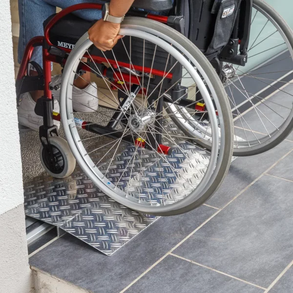 Eine Person im Rollstuhl fährt über eine Schwellenbrücke